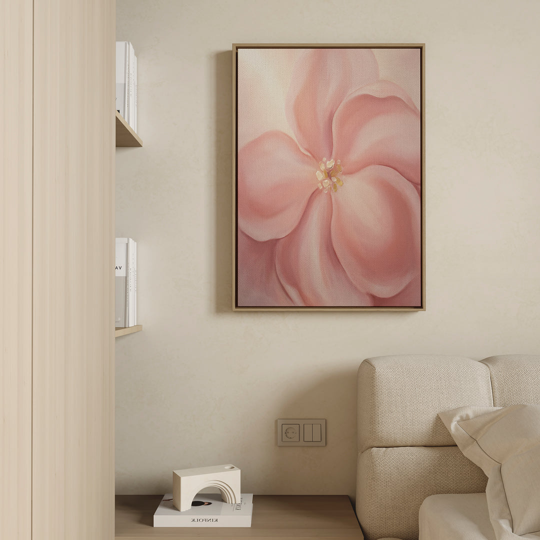 The Blushing Magnolia Canvas Art - Vertical hangs on a beige wall above a light sofa, while a floor shelf with books and a geometric white object completes the softly lit, minimalistic scene with romantic charm.