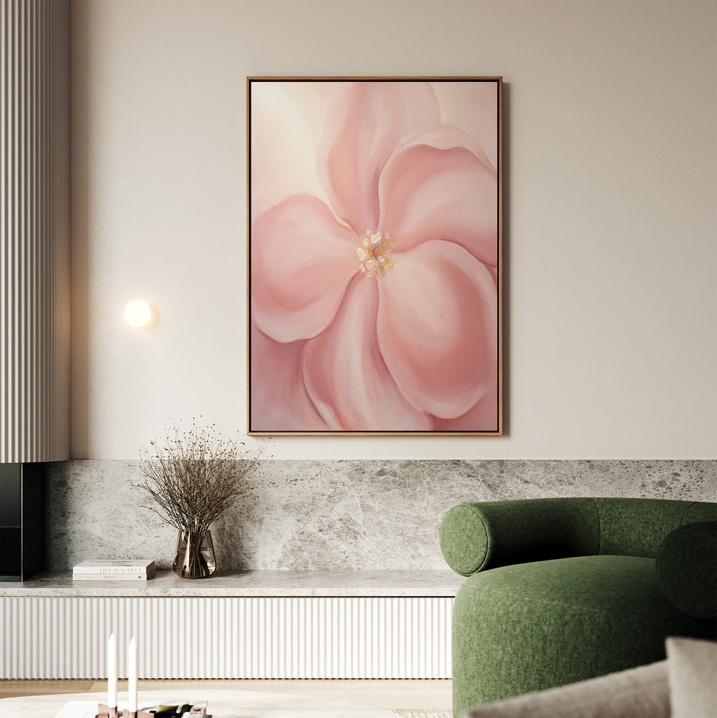 A living room featuring the Blushing Magnolia Canvas Art - Vertical, a green curved sofa, a vase with dried branches on a marble shelf, and neutral décor in earthy tones creates a softly romantic atmosphere.