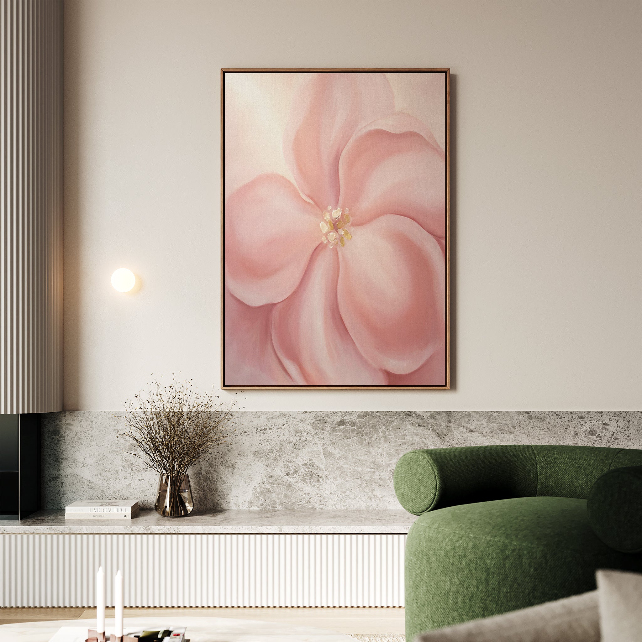 A living room featuring the Blushing Magnolia Canvas Art - Vertical, a green curved sofa, a vase with dried branches on a marble shelf, and neutral décor in earthy tones creates a softly romantic atmosphere.