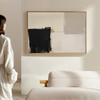 A person stands in a minimal, modern living room featuring a textured beige sofa and the Bold Division Canvas Art - Horizontal in black, white, and gray on the wall.