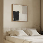 A minimalist bedroom features a beige upholstered bed with four cream pillows, and the Bold Division Canvas Art - Square in black and white above the headboard. A branch in a vase decorates the bedside table.