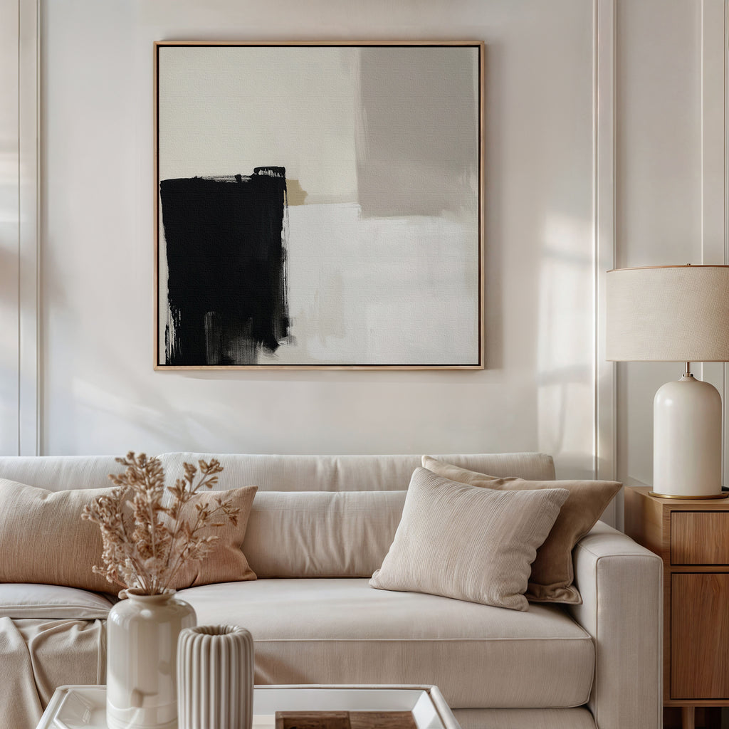 A modern living room featuring a beige sofa, neutral pillows, a wooden side table with a ceramic lamp, dried flowers in a vase, and the Bold Division Canvas Art - Square on the wall elevates contemporary style.