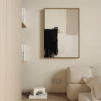 A minimalist interior features a beige couch, a light wood shelf with books and a sculpture, and the Bold Division Canvas Art - Vertical in black, white, and beige on a cream wall above electrical outlets.