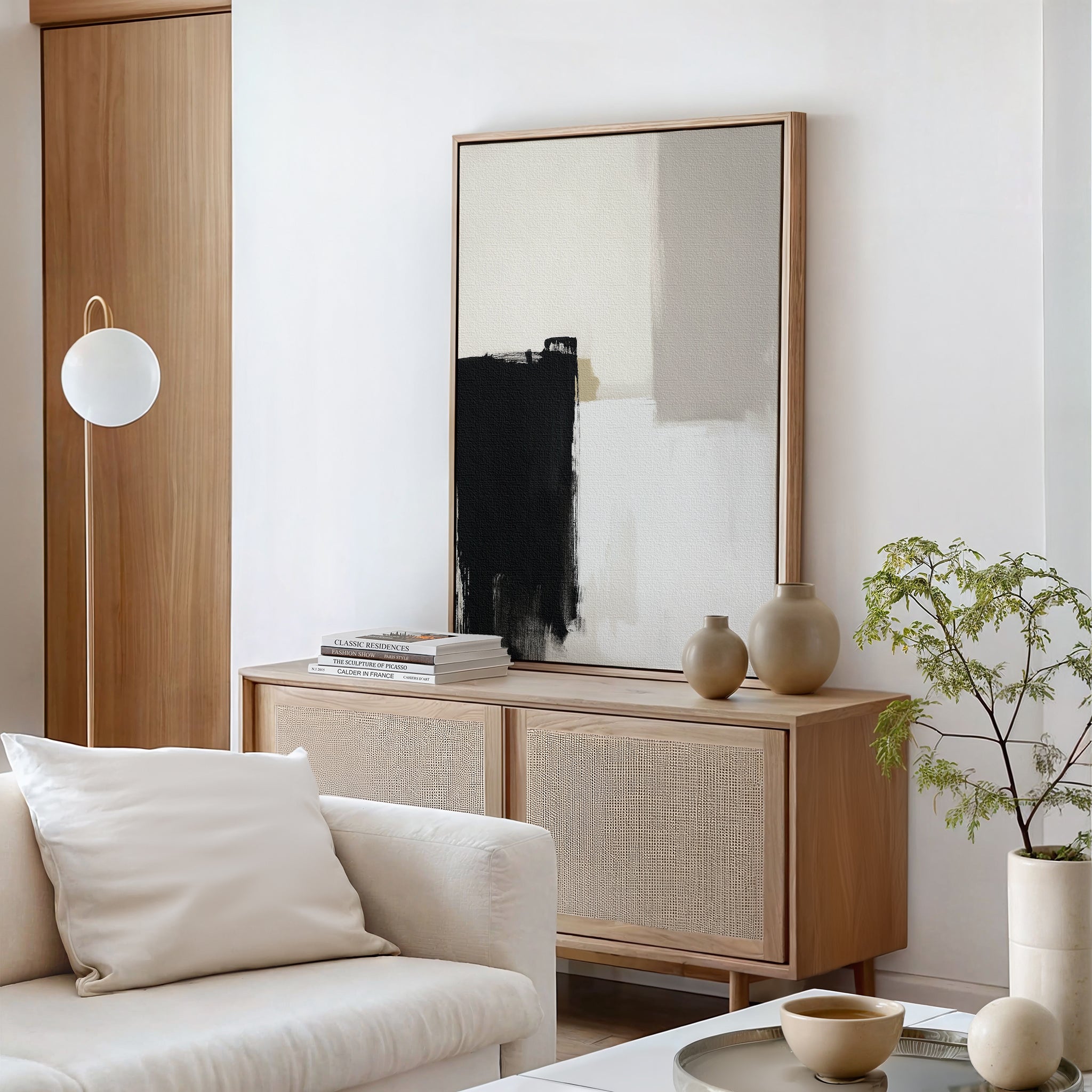 Minimalist living room with a light wood sideboard, Bold Division Canvas Art - Vertical, ceramic vases, a stack of books, a small green plant, a white cushioned sofa, and a modern round pendant light—ideal for modern decor lovers.
