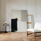 Minimalist interior with herringbone wood floor, a white cushioned chair, side table, and candles—perfect for modern living rooms. Two large canvases, including the Bold Division Canvas Art - Vertical, lean against the white paneled wall.