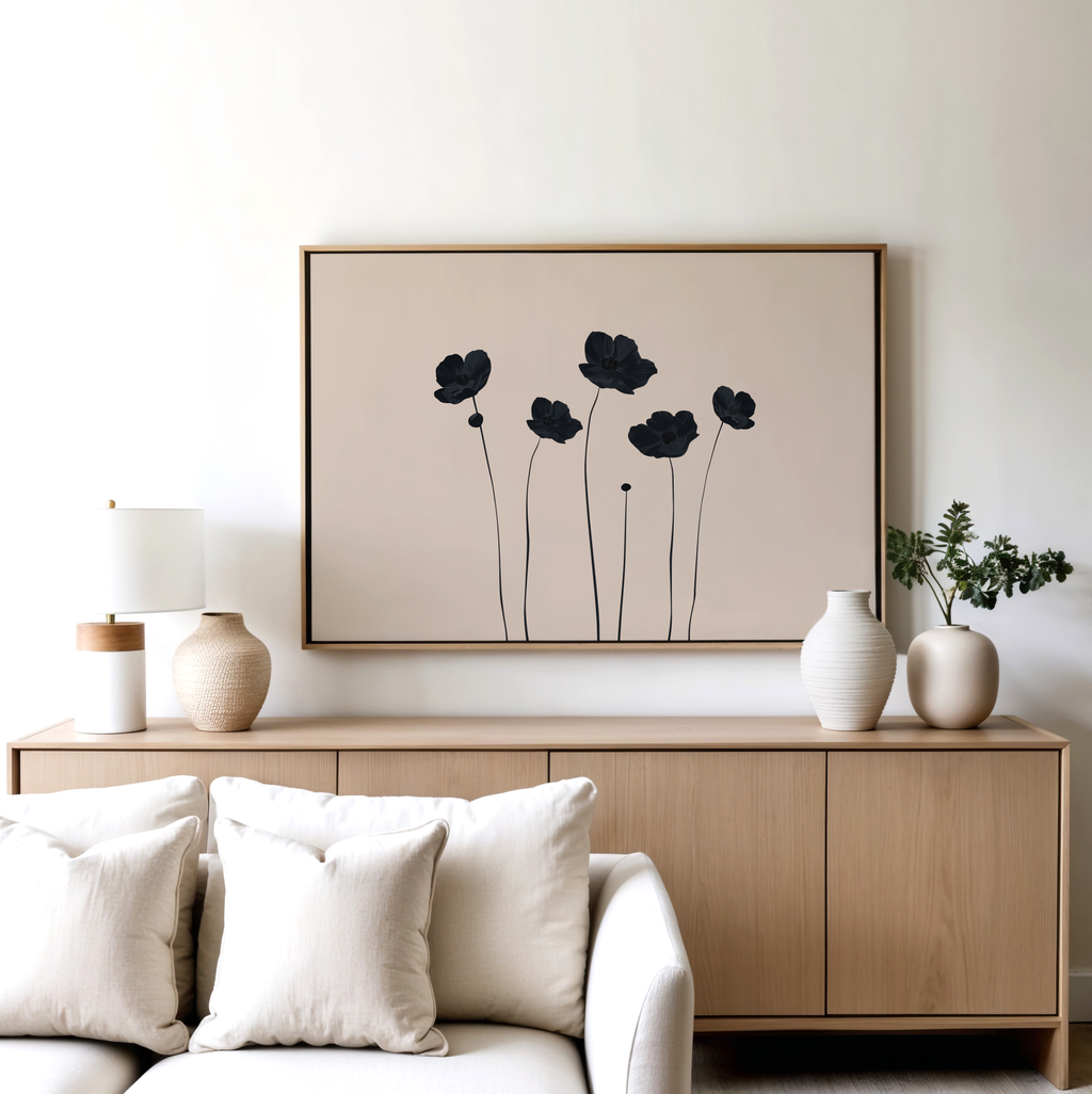 A modern living room with a light wood sideboard, neutral vases, a lamp, a plant, and the Botanic Abstract Canvas Art—a black minimalist floral print—framed above, paired with a white sofa and cream cushions in front.
