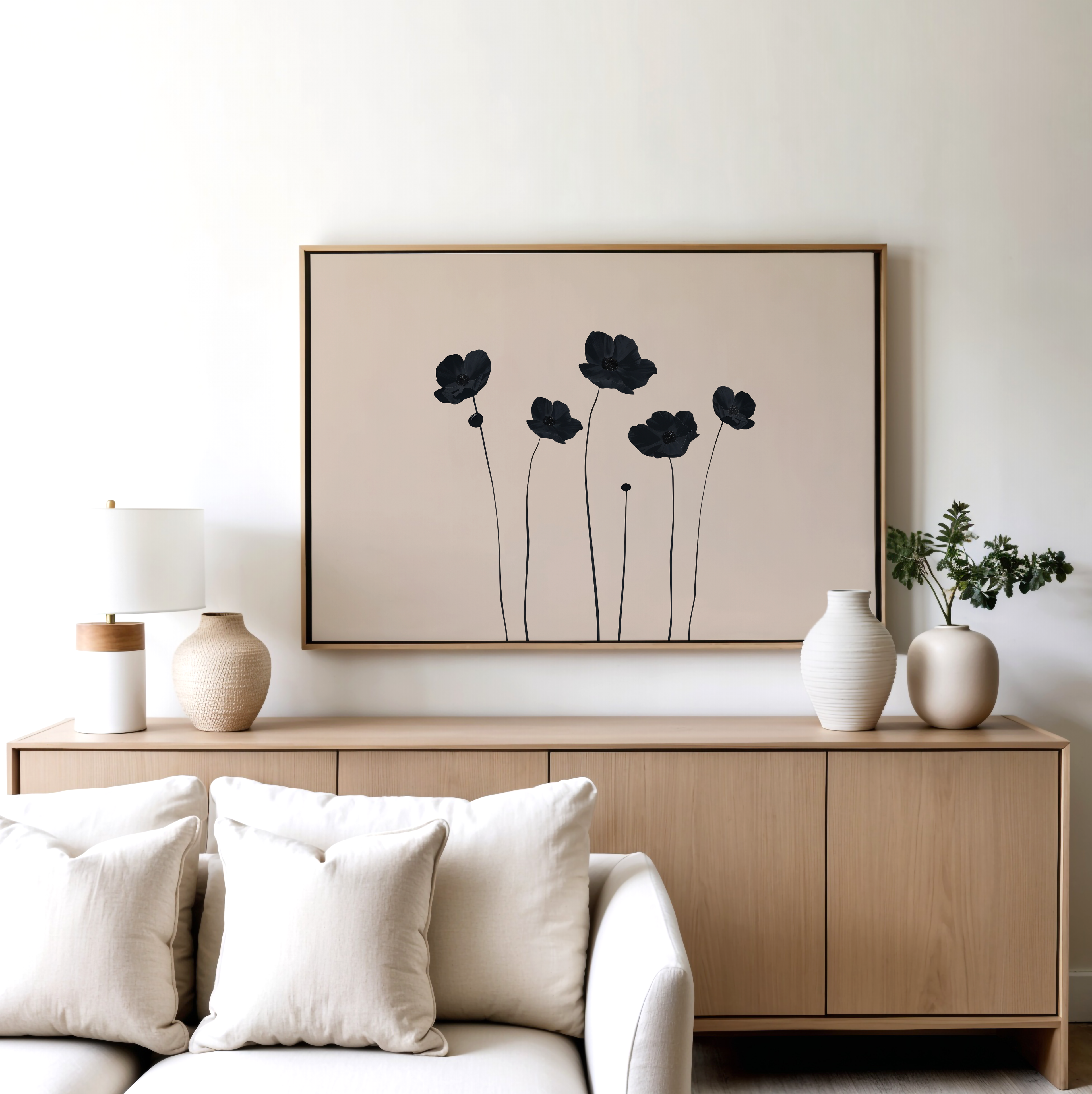 A modern living room with a light wood sideboard, neutral vases, a lamp, a plant, and the Botanic Abstract Canvas Art—a black minimalist floral print—framed above, paired with a white sofa and cream cushions in front.
