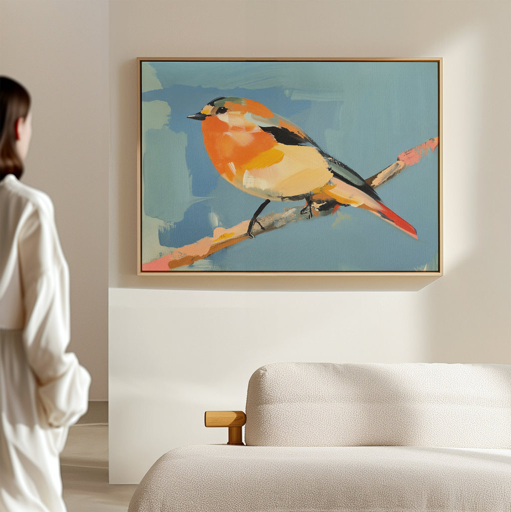 A person stands in a softly lit room, admiring the Bright Songbird Canvas Art - Horizontal, featuring an orange and yellow bird on a branch, displayed above a light-colored sofa.