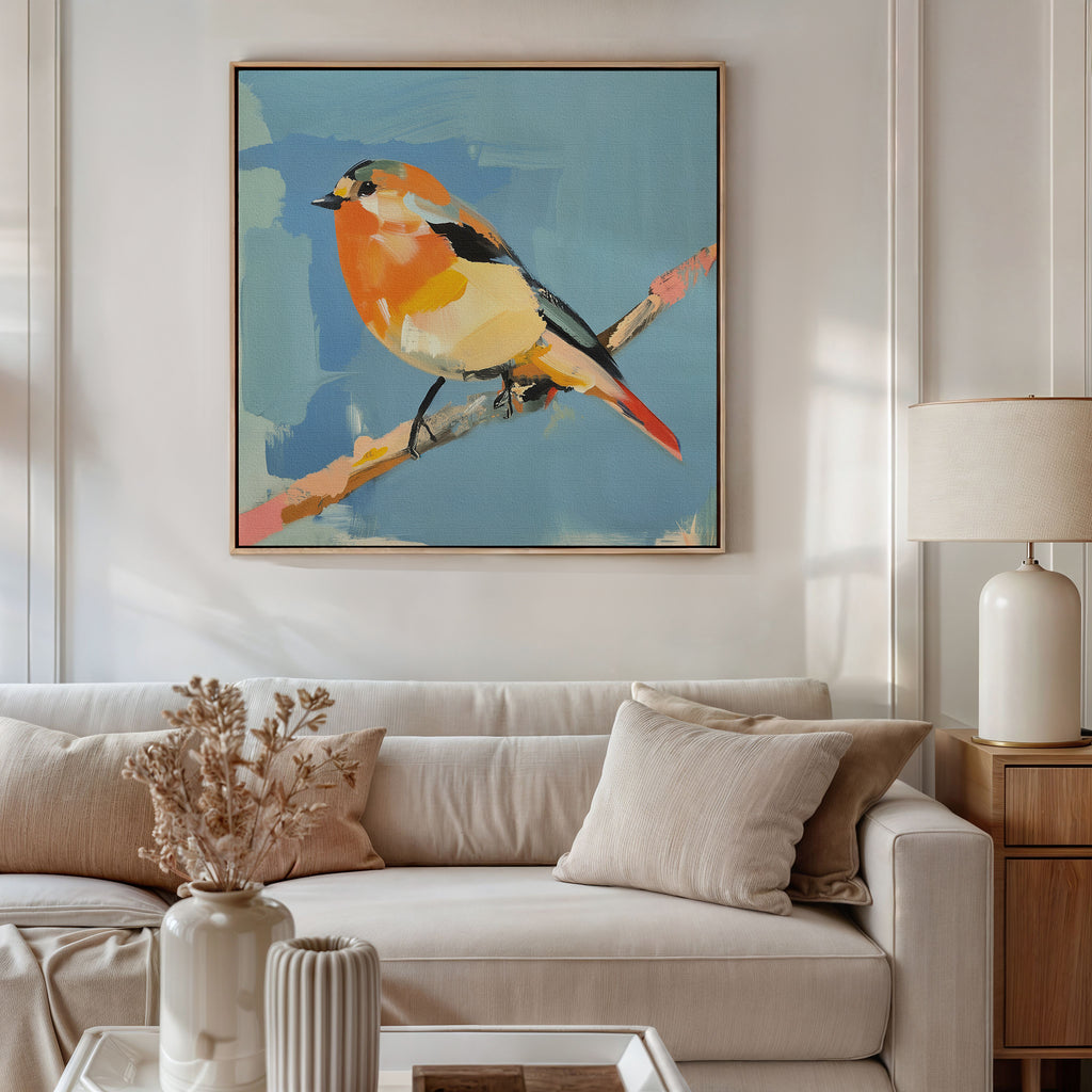 A modern living room with a beige sofa and neutral pillows features the Bright Songbird Canvas Art - Square, a colorful painting of a bird on a branch against blue, hung above the sofa. Dried flowers and a table lamp complete the decor.