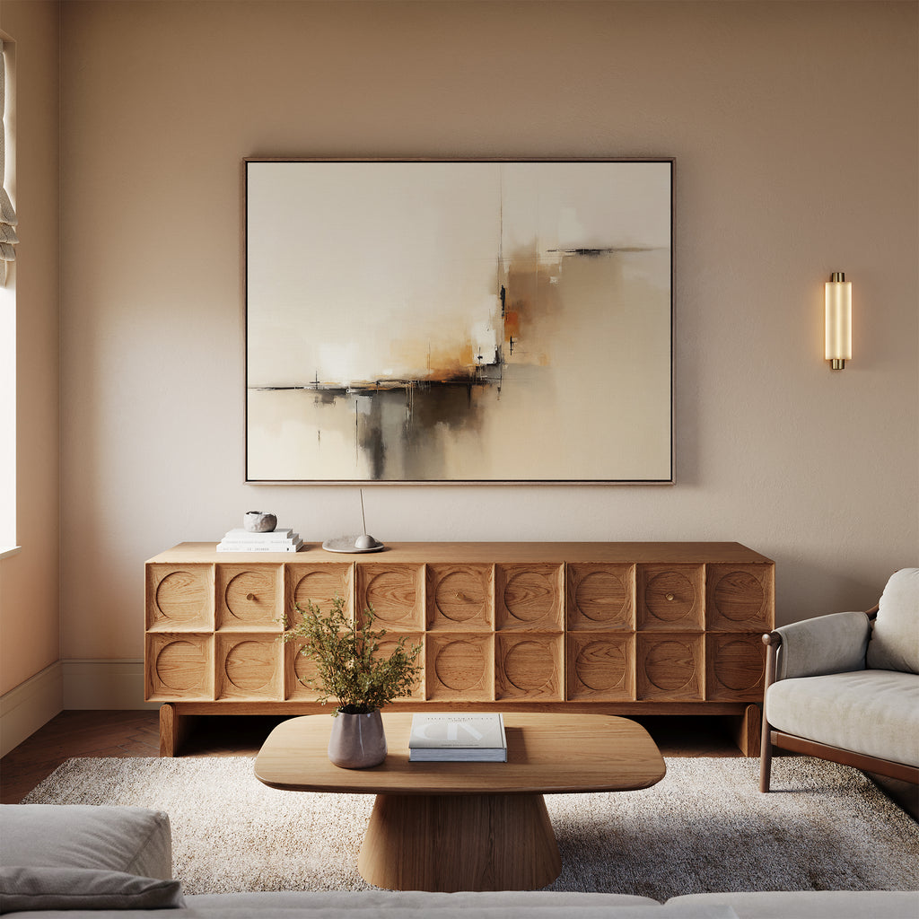 A modern living room in neutral tones features a wooden sideboard with circular patterns, topped by the Burnt Sienna Convergence Canvas Art - Horizontal, a light wood coffee table, floral vase accents, and cozy seating on a plush rug.