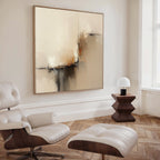 A modern, minimalist living room with a white lounge chair and ottoman, Burnt Sienna Convergence Canvas Art - Square as wall art, a geometric wooden side table, and a small white lamp on herringbone wood flooring.