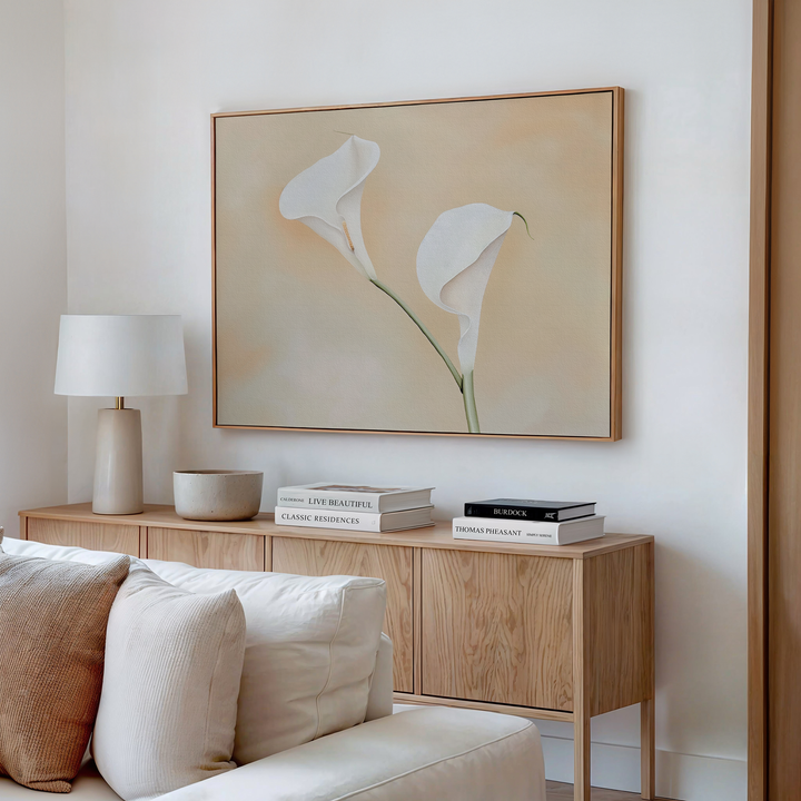 A minimal, modern living room features a light wood sideboard, white sofa, books, a lamp, a bowl, and the Calla Serenity Abstract Canvas Art. Neutral tones and this minimalist wall art create a calm, elegant atmosphere.