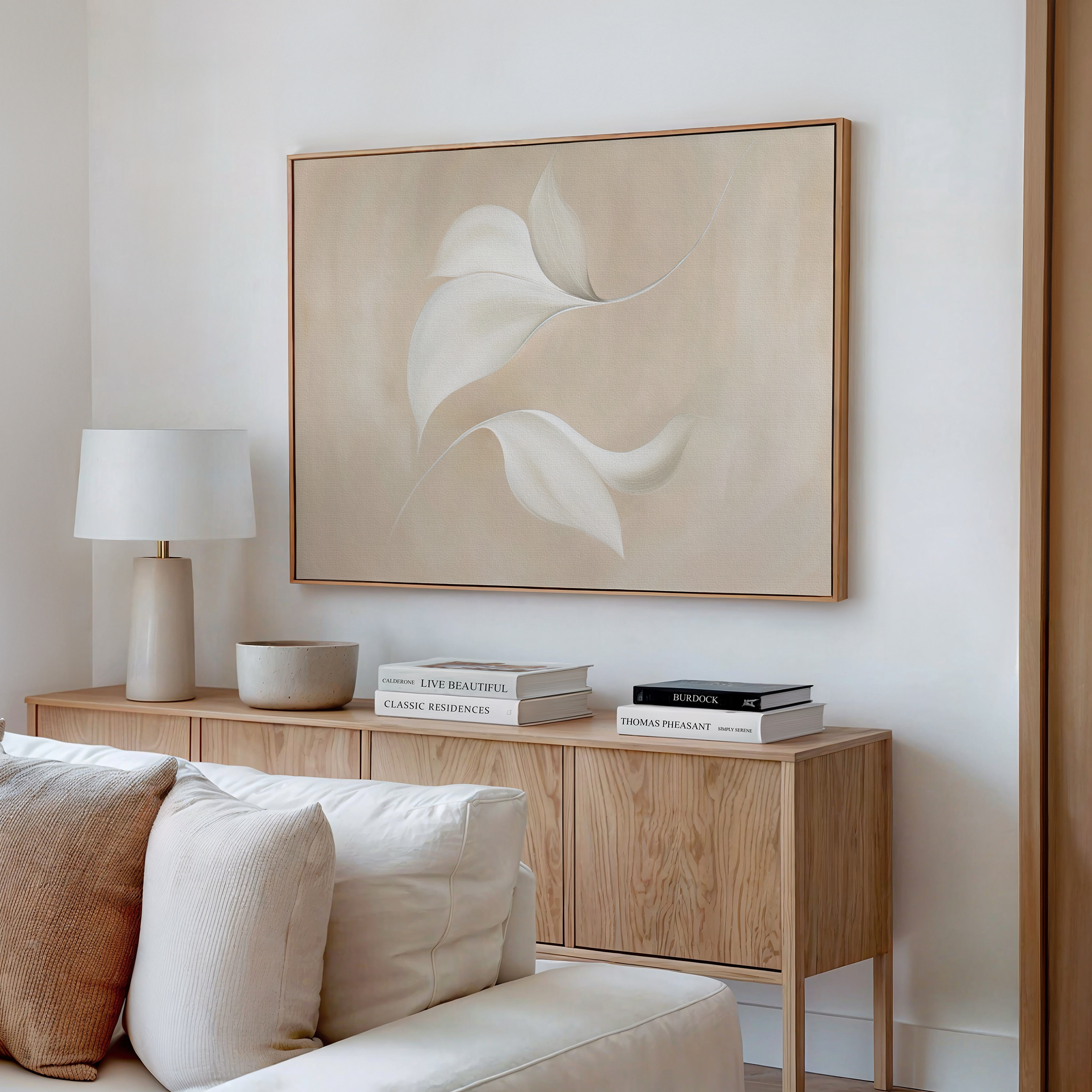 A modern, minimalist living room with a light wood sideboard, books, a lamp, a bowl, and the Garden Spectrum Abstract Canvas Art with soft leaf motifs above a white couch—perfect for elegant living room decor.