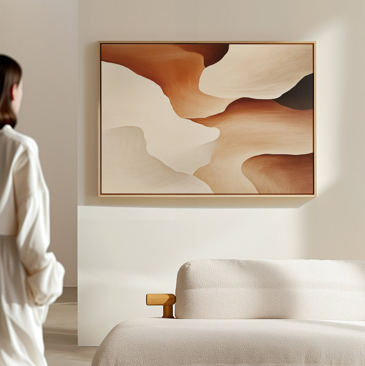 A woman in a white outfit stands in a modern, minimal living room, gazing at the Canyon Curves Canvas Art - Horizontal in warm earth tones hanging above a light-colored sofa.