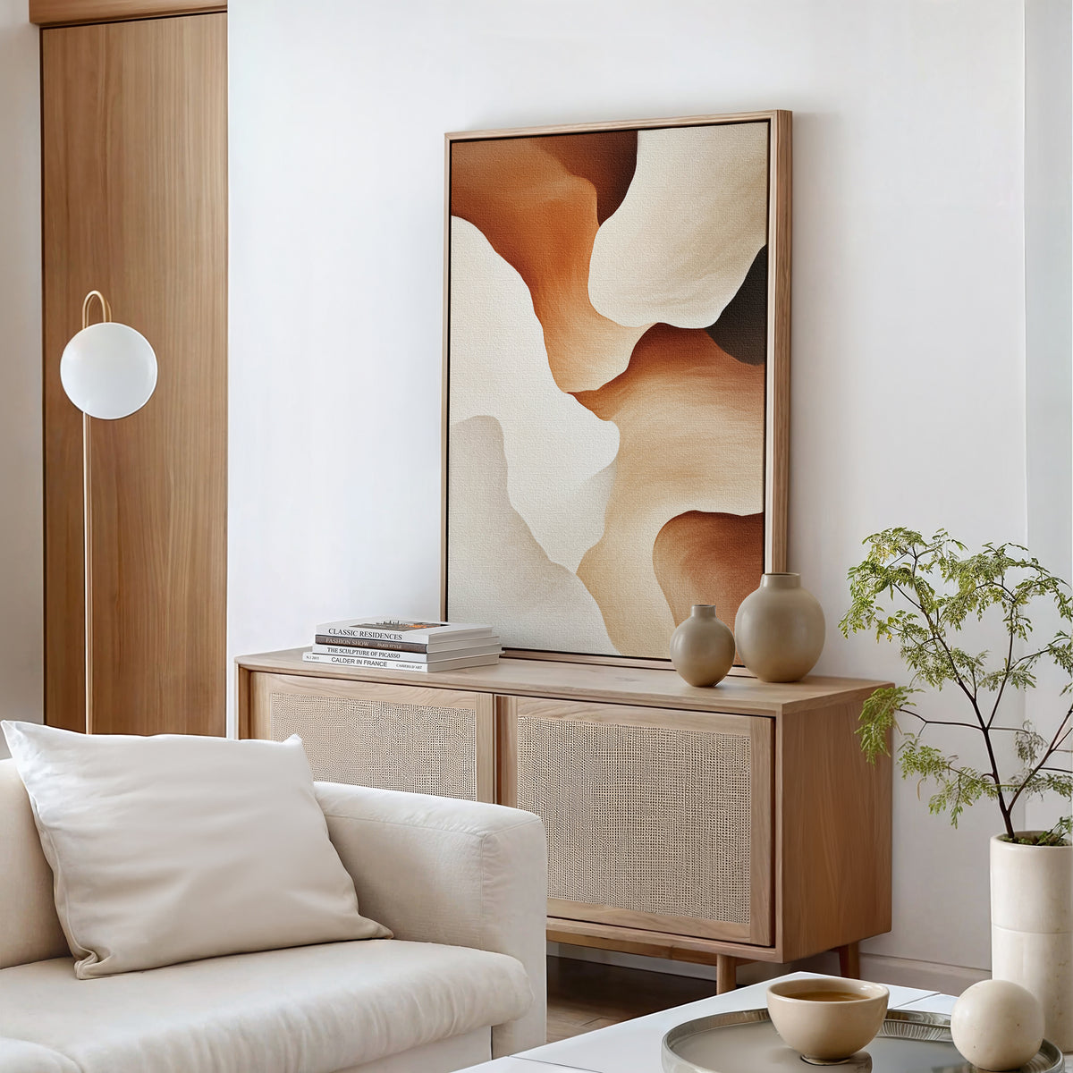 A modern, minimalist living room features a light wood sideboard with neutral vases, books, and the Canyon Curves Canvas Art - Vertical in warm earth tones. A white sofa, round lamp, and potted plant complete the airy, serene decor.
