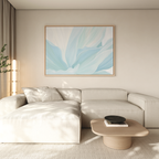 A modern living room with a light beige sectional sofa and neutral walls features the Icy Petals Abstract Canvas Art in blue and white above. A wooden coffee table holds books and a black bowl, while sunlight filters through sheer curtains.