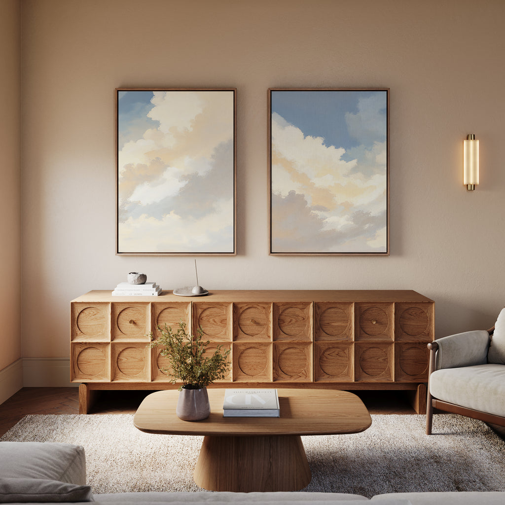 A modern living room with a wooden coffee table, patterned wood sideboard, the Celestial Embrace - Set of 2 cloud wall art prints, a beige armchair, and wall sconce—all in neutral tones for a calming Nordic Park vibe.
