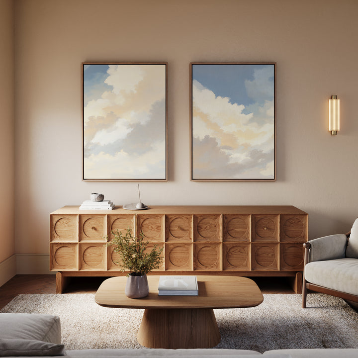 A modern living room with a wooden coffee table, patterned wood sideboard, the Celestial Embrace - Set of 2 cloud wall art prints, a beige armchair, and wall sconce—all in neutral tones for a calming Nordic Park vibe.
