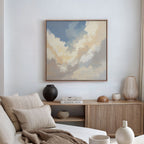 A cozy, modern living room with a neutral palette features a beige sofa, textured pillows, and a wooden console table adorned with books and ceramics. Above the table hangs the Celestial Embrace Canvas Art - Square for serene decor.
