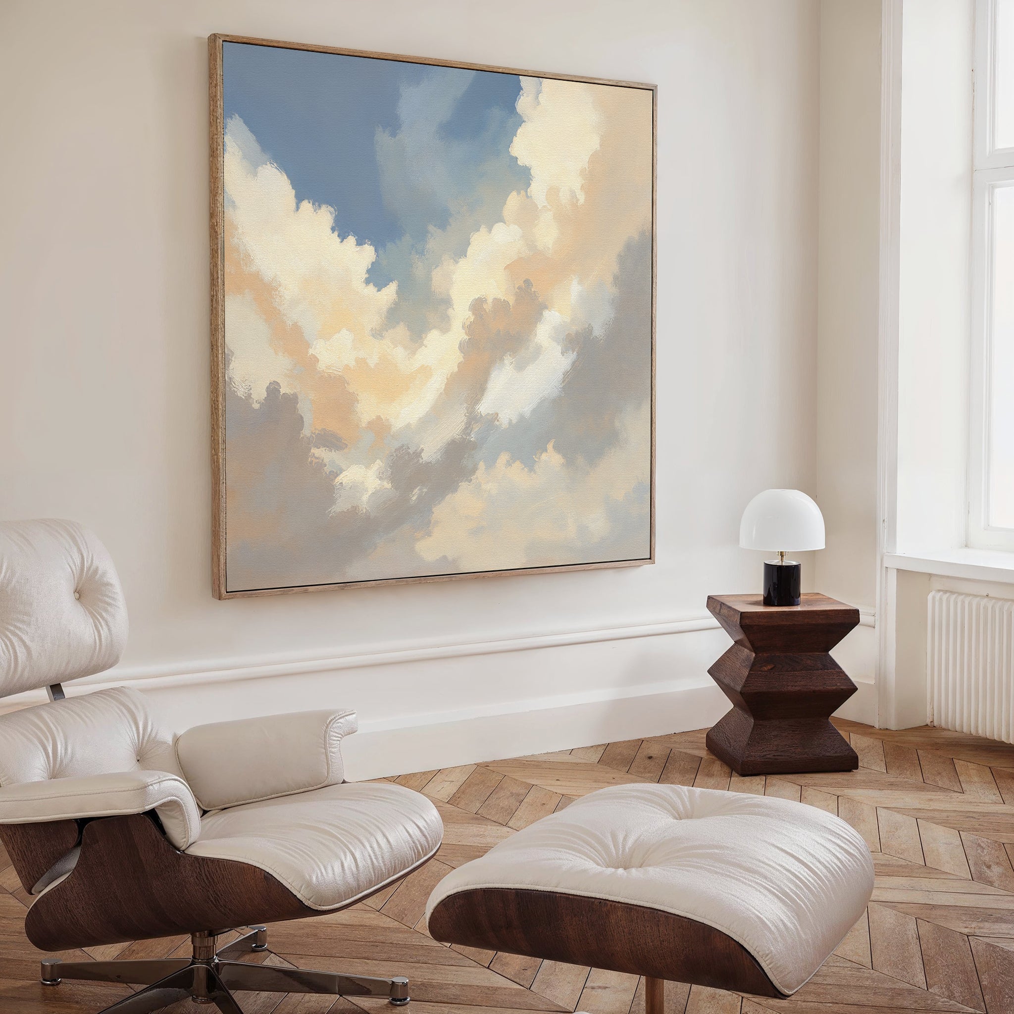 A modern living room features a white leather lounge chair with ottoman, wooden side table and lamp, and the Celestial Embrace Canvas Art - Square on the wall. Sunlight pours through a tall window, enhancing the serene decor.
