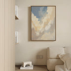 A soft, neutral living room corner features a beige sofa, books on a shelf, a modern white decorative piece, and the serene Celestial Embrace Canvas Art - Vertical—adding tranquility to this Nordic Park-inspired space.