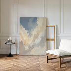 The Celestial Embrace Canvas Art - Vertical leans against a white paneled wall beside an empty frame. A modern white cushioned chair and round table with candles and a book set a serene mood on the herringbone wood floor.