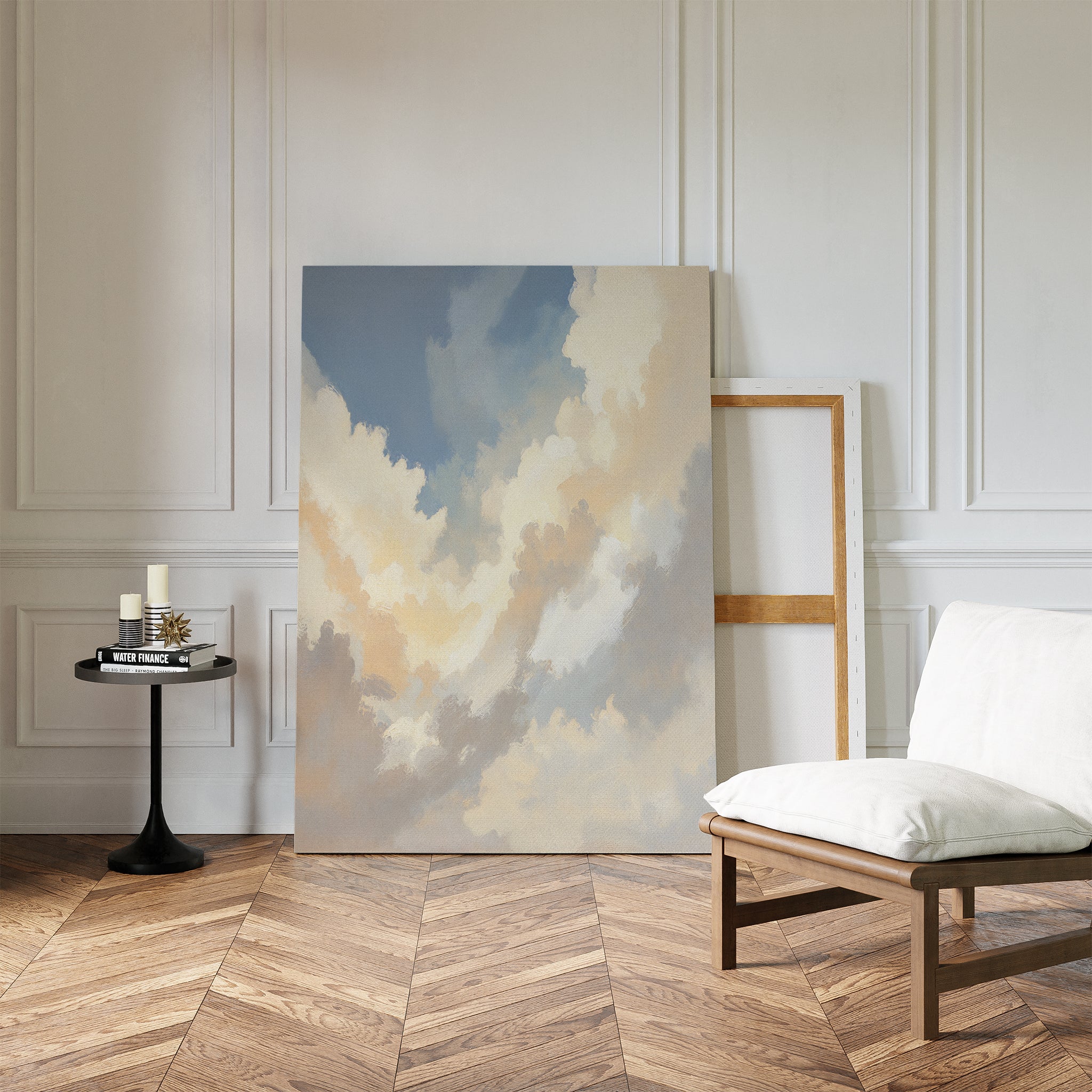 The Celestial Embrace Canvas Art - Vertical leans against a white paneled wall beside an empty frame. A modern white cushioned chair and round table with candles and a book set a serene mood on the herringbone wood floor.