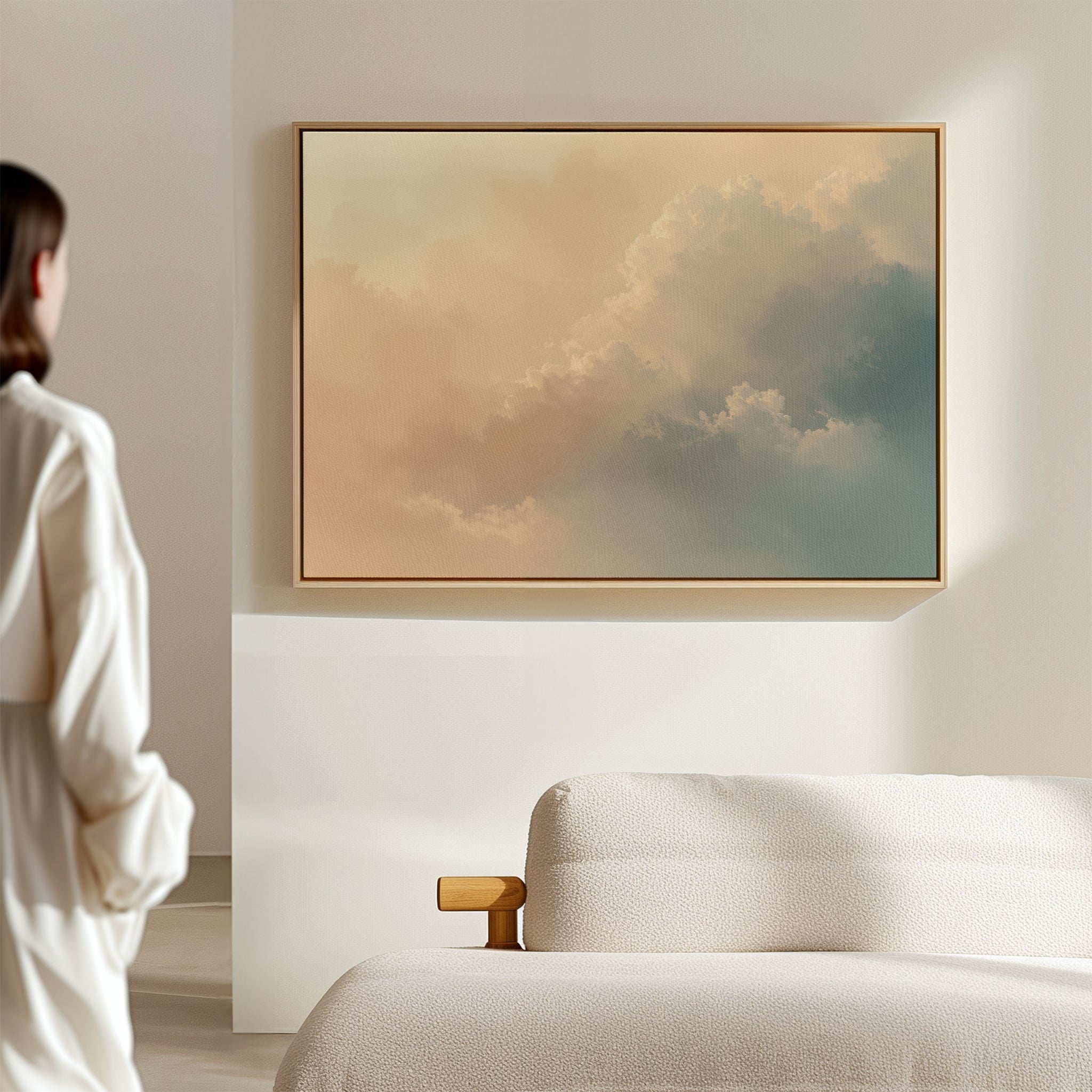 A person in white stands in a minimal, sunlit room featuring champagne light, a beige sofa, and the Celestial Veil Canvas Art - Horizontal with soft pastel clouds hanging on the wall.