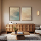 A modern living room with a wooden sideboard and coffee table, beige walls, a set of two Celestial Veil canvas prints, a wall sconce casting champagne light, a neutral armchair, and a small vase with greenery on the coffee table.