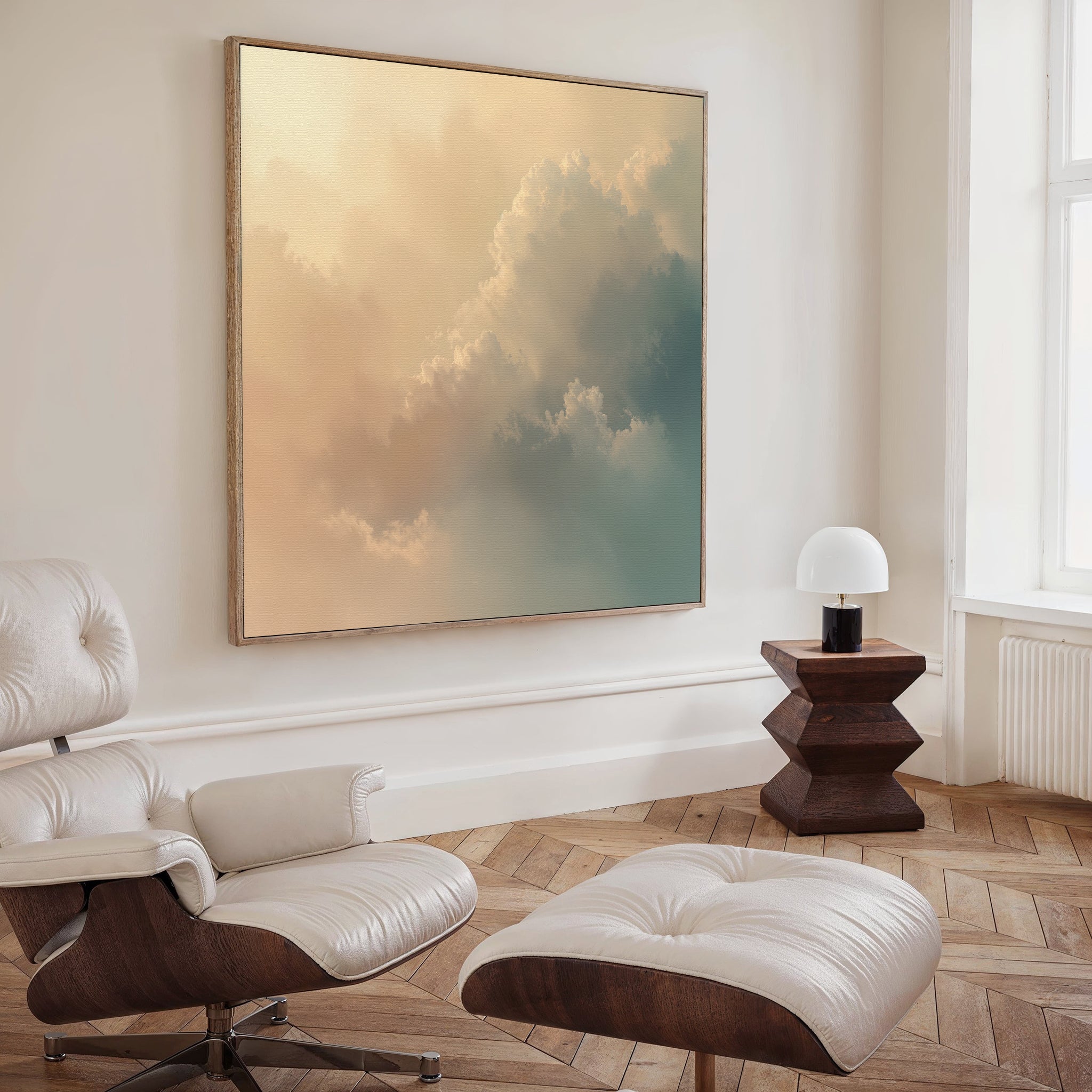 A minimal modern living room features a white lounge chair and ottoman, a wooden side table with a lamp, and the Celestial Veil Canvas Art - Square on the wall above light wood herringbone floors bathed in champagne light.