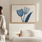 A person in a light robe stands by a beige sofa, admiring the Cerulean Tulips Canvas Art - Horizontal on a white wall in a softly lit, minimalist room inspired by Nordic Park.