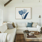 A cozy living room with a white sectional, assorted pillows, a rustic wooden coffee table, and the Cerulean Tulips Canvas Art - Horizontal on the wall. White shiplap walls create a Nordic Park-inspired vibe.
