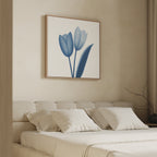 A beige bedroom features a neatly made bed with four white pillows and the Cerulean Tulips Canvas Art - Square above the headboard. A bare branch in a vase sits on the side table next to the bed.