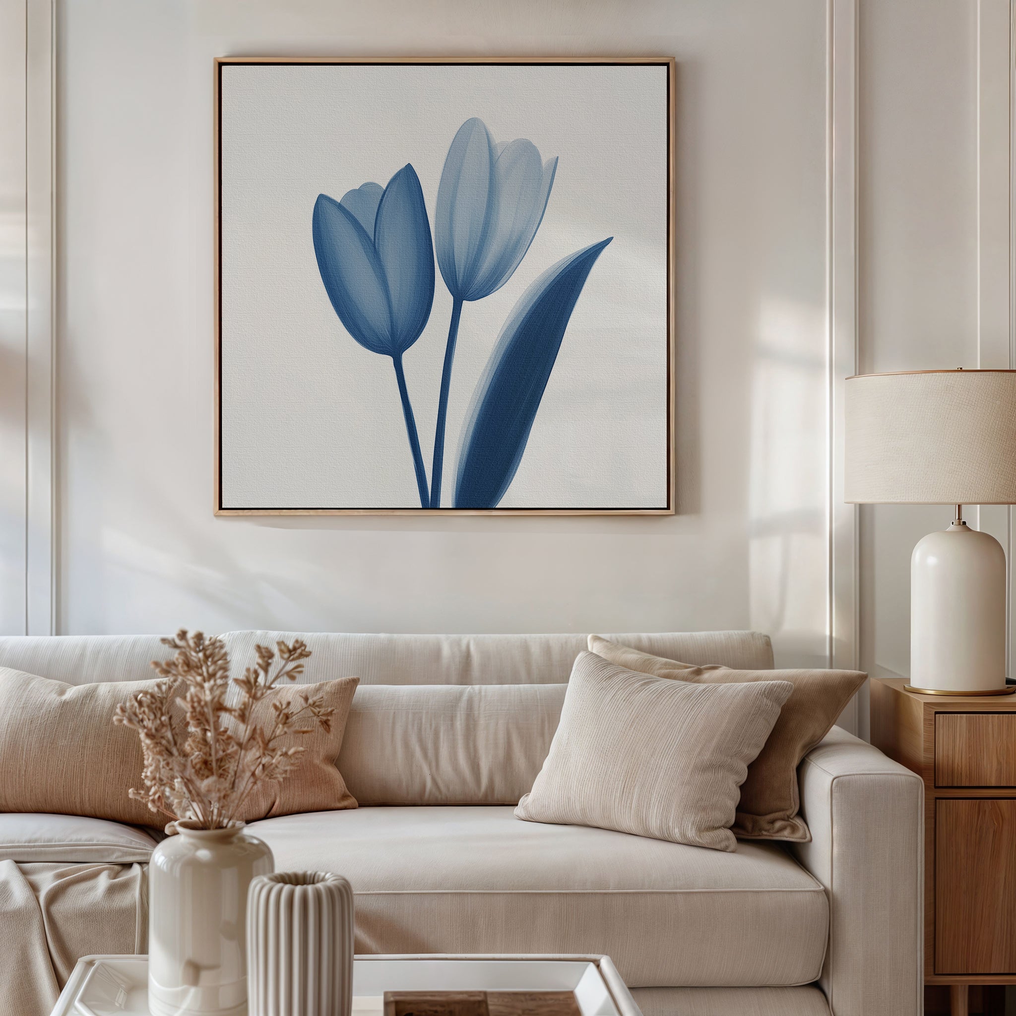 A modern living room features a beige sofa, neutral cushions, a dried floral arrangement on the coffee table, a table lamp, and the Cerulean Tulips Canvas Art - Square displayed above the couch.