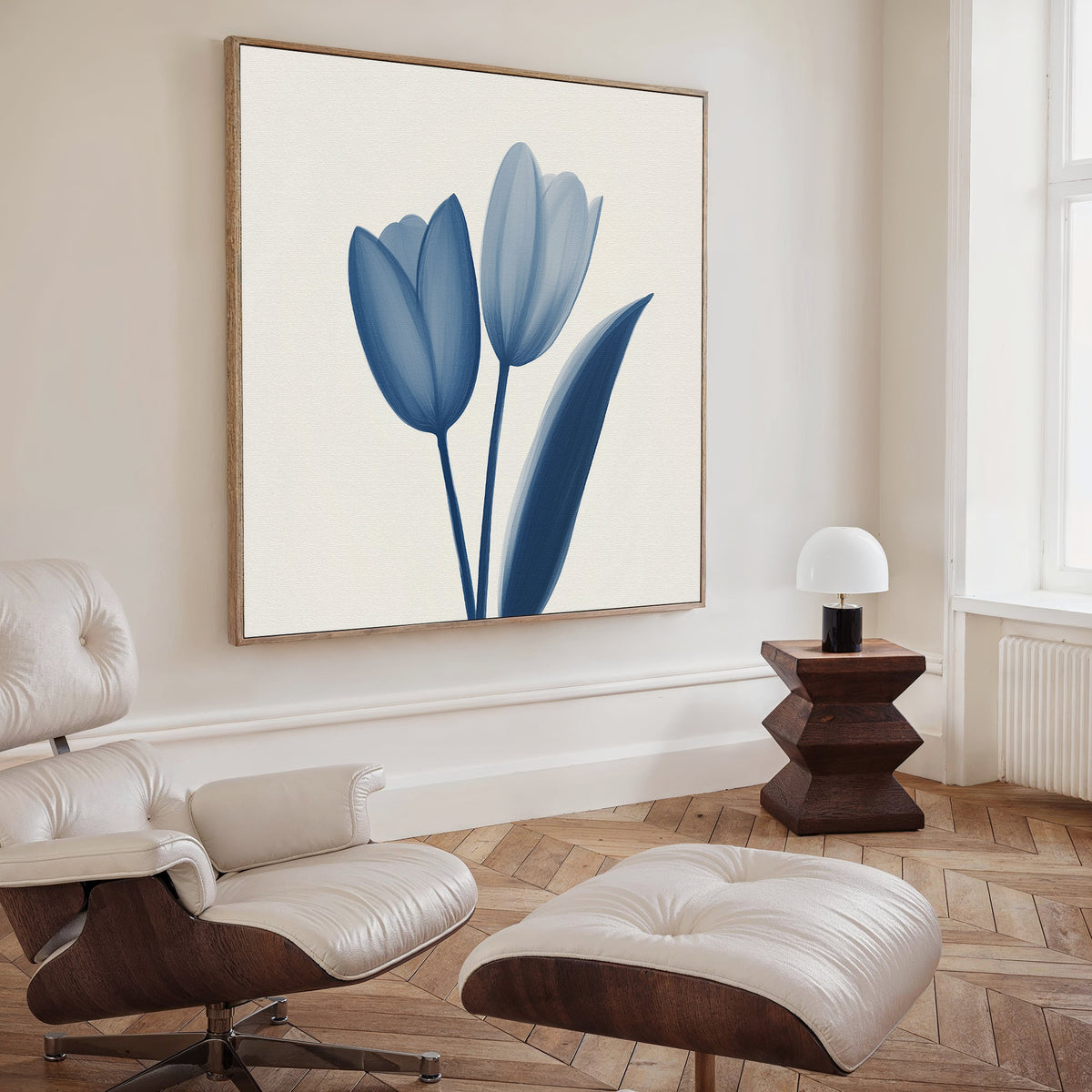 A modern living room features a white lounge chair and ottoman, a wooden side table with a small white lamp, and the Cerulean Tulips Canvas Art - Square as a bold botanical accent on a cream-colored wall inspired by Nordic Park style.