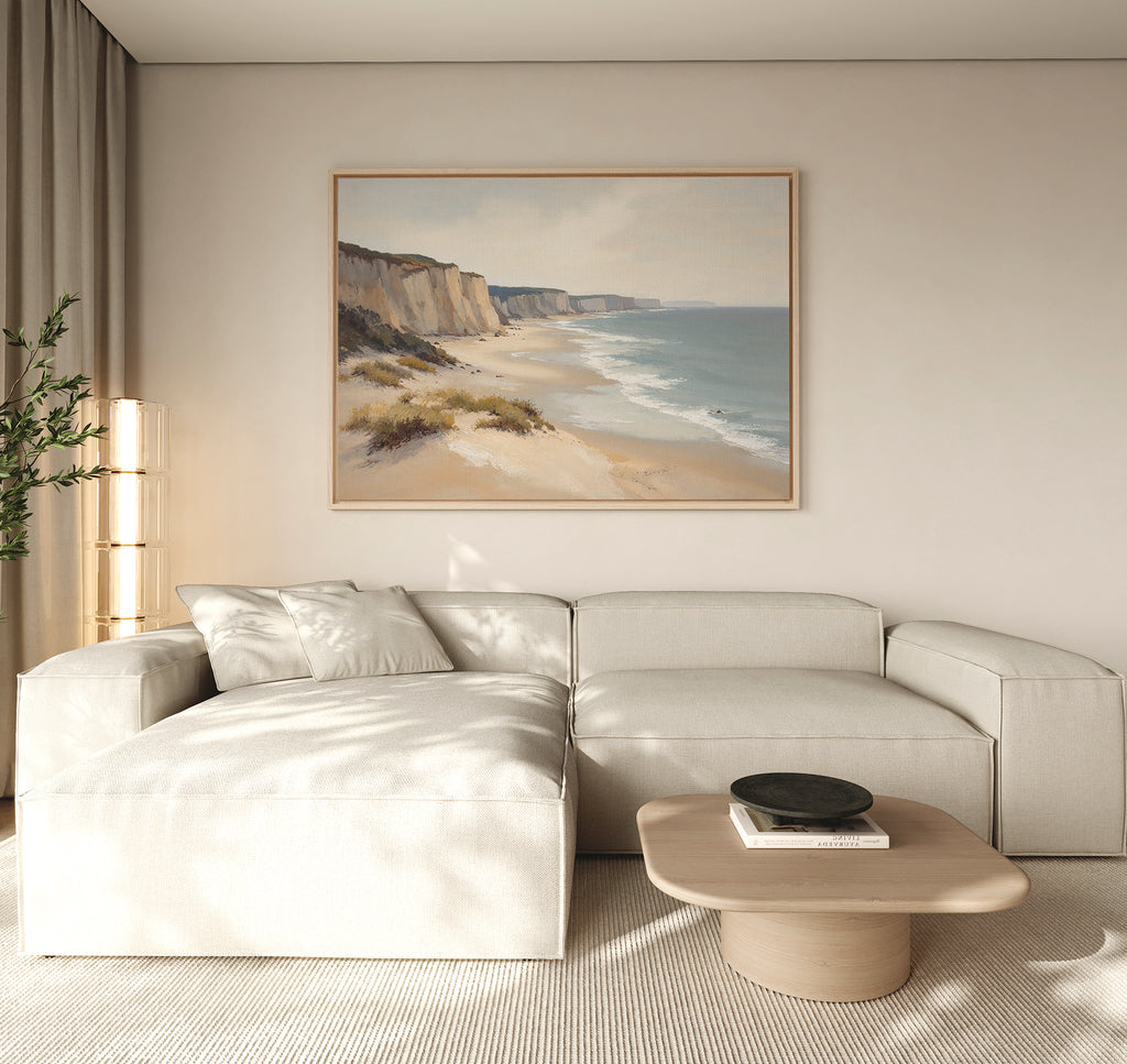 A modern living room with a light beige sectional sofa, a low wooden coffee table with a black bowl, a tall lamp, a potted plant, and striking coastal wall art—the Chalk Shores Canvas Art - Horizontal—displayed on the wall.