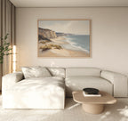 A modern living room with a light beige sectional sofa, a low wooden coffee table with a black bowl, a tall lamp, a potted plant, and striking coastal wall art—the Chalk Shores Canvas Art - Horizontal—displayed on the wall.
