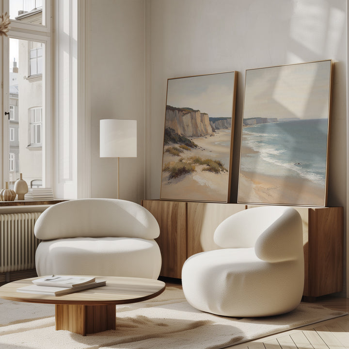 A modern living room features the Chalk Shores - Set of 2 curved white armchairs, a low wooden coffee table, and a sideboard with seaside wall art. Sunlight streams through tall windows, evoking a bright Nordic Park vibe.
