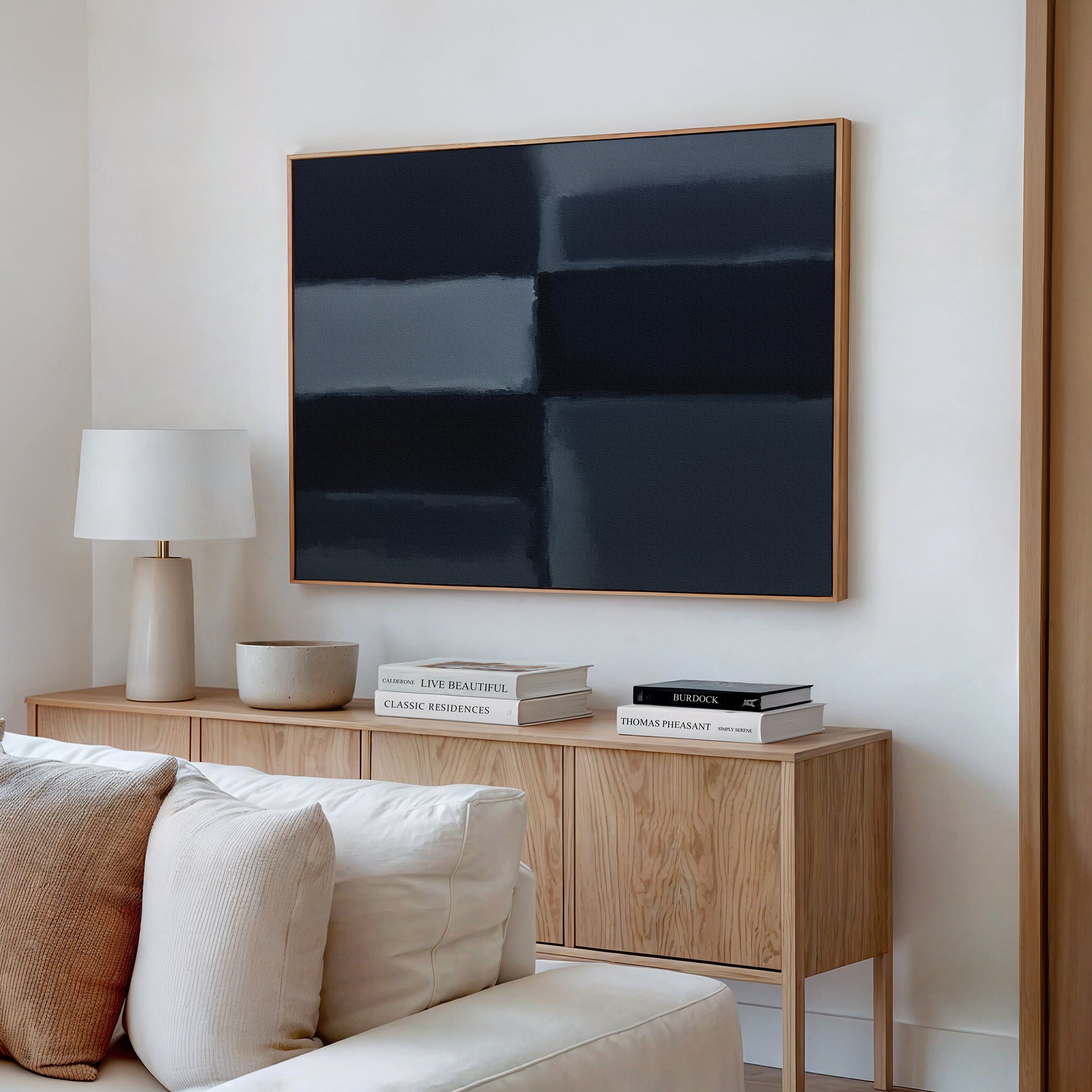 A modern living room featuring a light wood sideboard, white table lamp, stacked books, decorative bowls, cream sofa, and the Charcoal Blocks Canvas Art - Horizontal as striking geometric wall decor.