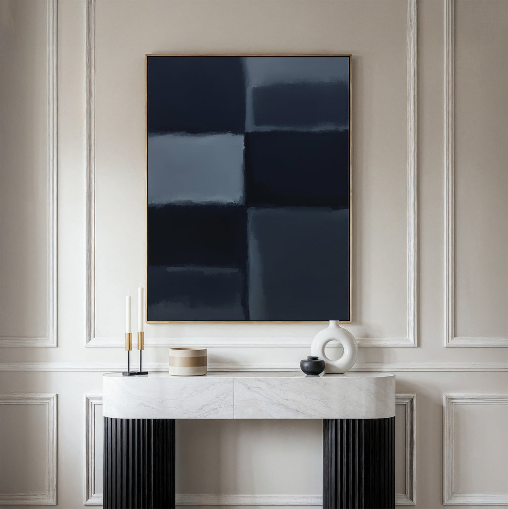 A minimalist console table with a marble top displays modern decor beneath the Charcoal Blocks Canvas Art - Vertical in dark blue hues, all set against an elegant, light-paneled wall.