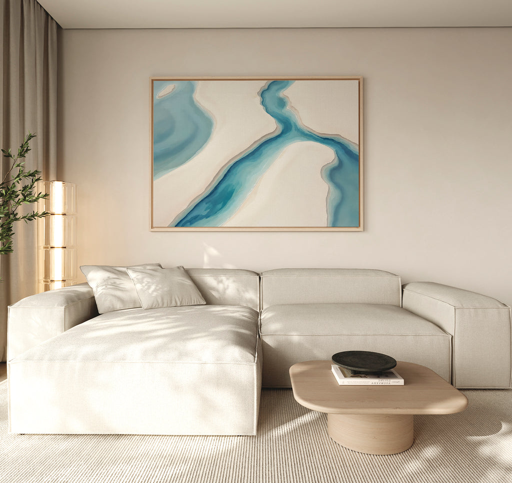 A modern living room with a light beige sectional sofa, a pale wood coffee table with a black bowl, a tall plant, and the 'Coastal Dreams Canvas Art - Horizontal' displayed above the sofa.