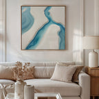 A modern living room with a beige sofa, light cushions, a wooden side table, cream lamp, dried flowers in a vase, and the Coastal Dreams Canvas Art - Square featuring blue and white shapes displayed above the couch.