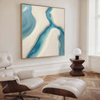 A modern living room featuring a cream leather lounge chair and ottoman, a wooden side table with a white lamp, and the Coastal Dreams Canvas Art - Square showcasing blue and beige shapes for a calming ambiance.