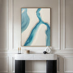 A modern minimalist room features a white console table with black legs, decorative objects, and the Coastal Dreams Canvas Art - Vertical above, displaying blue and beige flowing shapes for a serene touch.