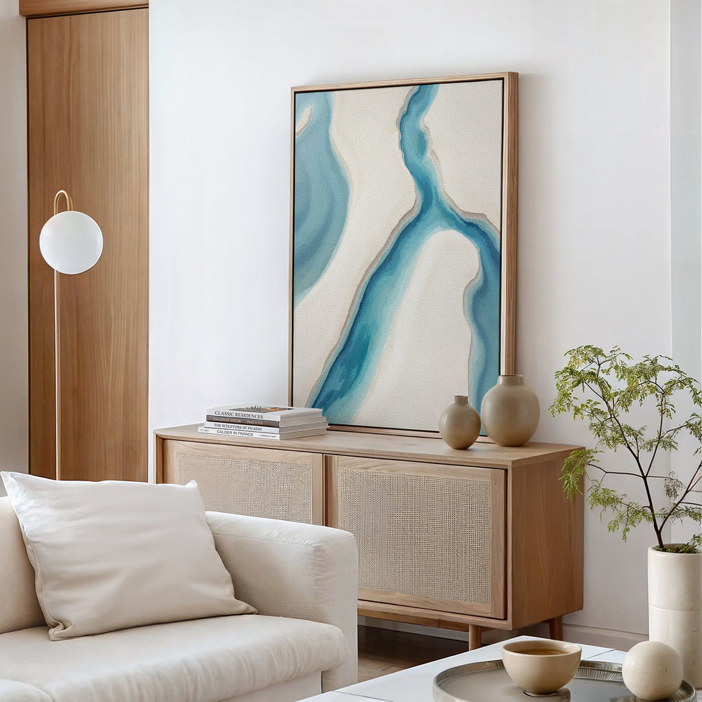 Minimalist living room featuring the Coastal Dreams Canvas Art - Vertical, a light wood cabinet, neutral vases, potted plant, white sofa with cushion, and modern round light fixture for serene coastal-inspired decor.