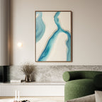 A modern living room features a green sofa, marble and wood paneling, and the "Coastal Dreams Canvas Art - Vertical" with blue and beige shapes above a low shelf with a vase of dried branches for serene decor.