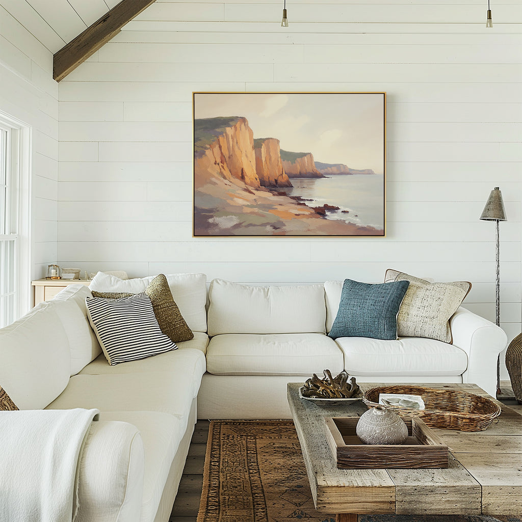 A cozy living room with a white sectional, assorted throw pillows, a rustic wood coffee table with decor, and the Coastal Grandeur Canvas Art - Horizontal of cliffs displayed on a white shiplap wall.