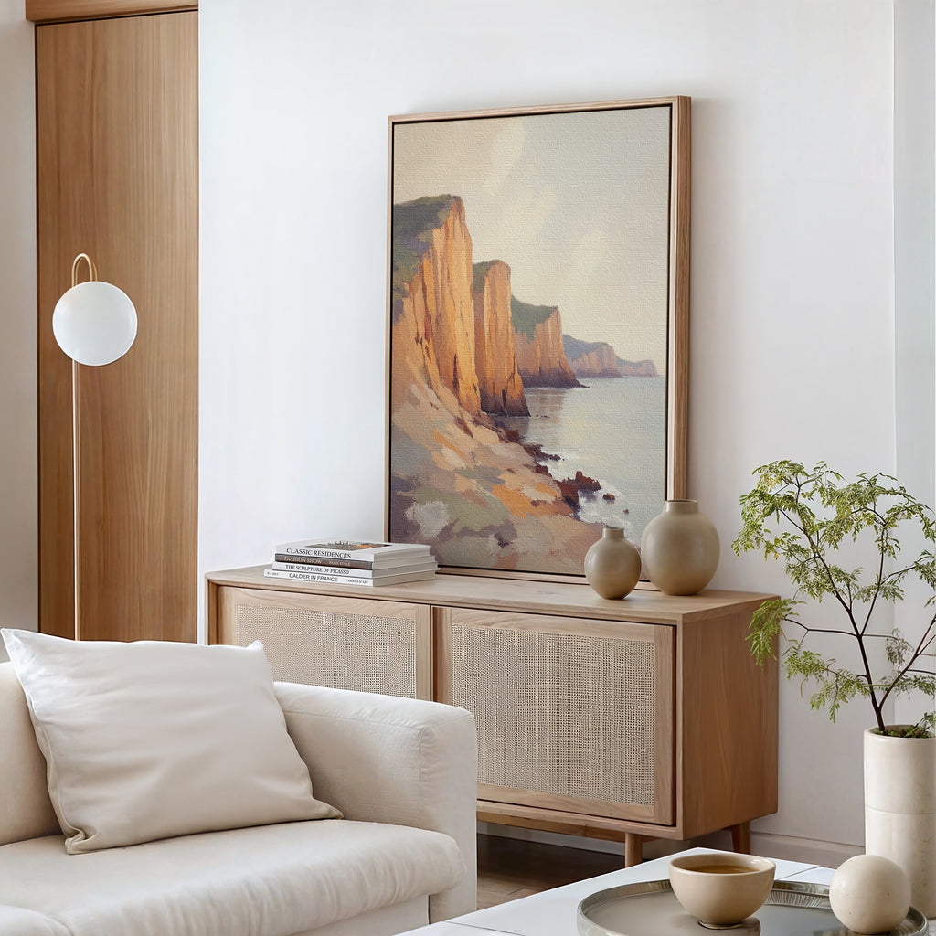 A modern living room in neutral tones featuring a wooden sideboard, ceramic vases, books, a potted plant, and the Coastal Grandeur Canvas Art - Vertical depicting seaside cliffs hanging above the sideboard.