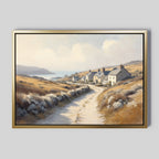 The Coastal Haven Canvas Art - Horizontal features a framed rustic landscape with a winding dirt road, cottages, rolling hills, and the sea beneath a partly cloudy sky.