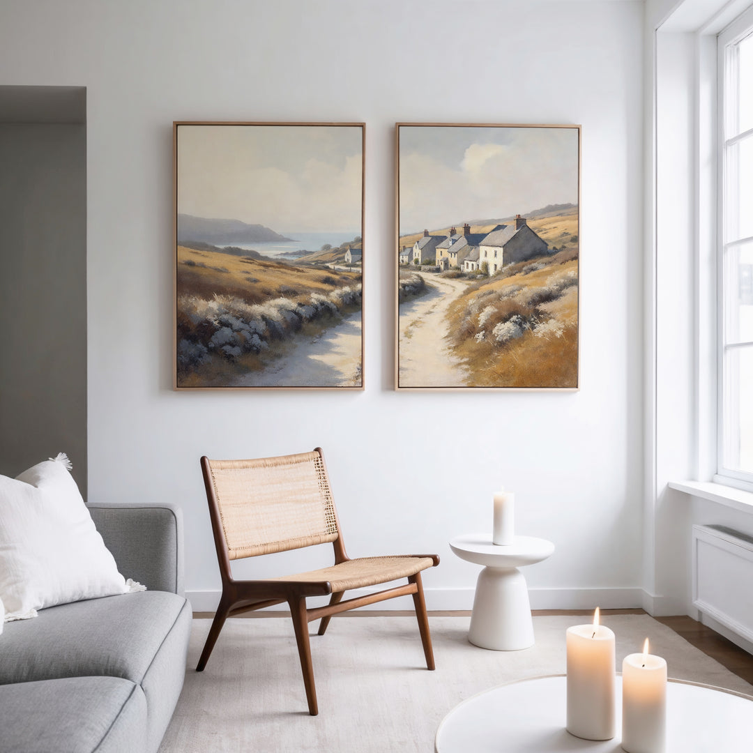 A modern living room features a woven chair, round side table, lit candles, and the "Coastal Haven - Set of 2" landscape canvas prints above. Natural light from large windows enhances the rustic charm and serenity of the space.